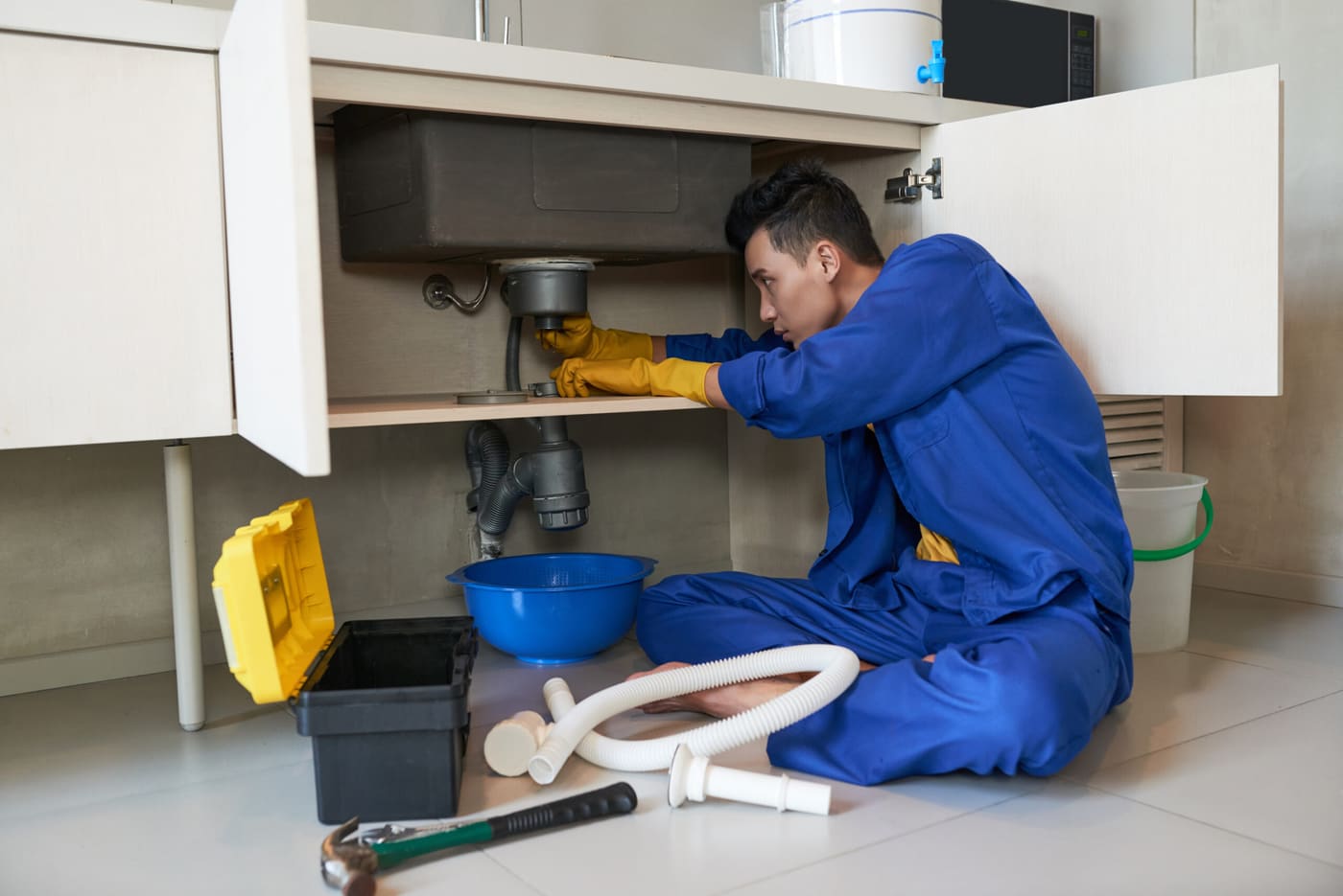 Plumber in blue overalls clearing a sink drain trap.