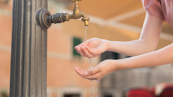 Young woman getting water from a faucet outdoors