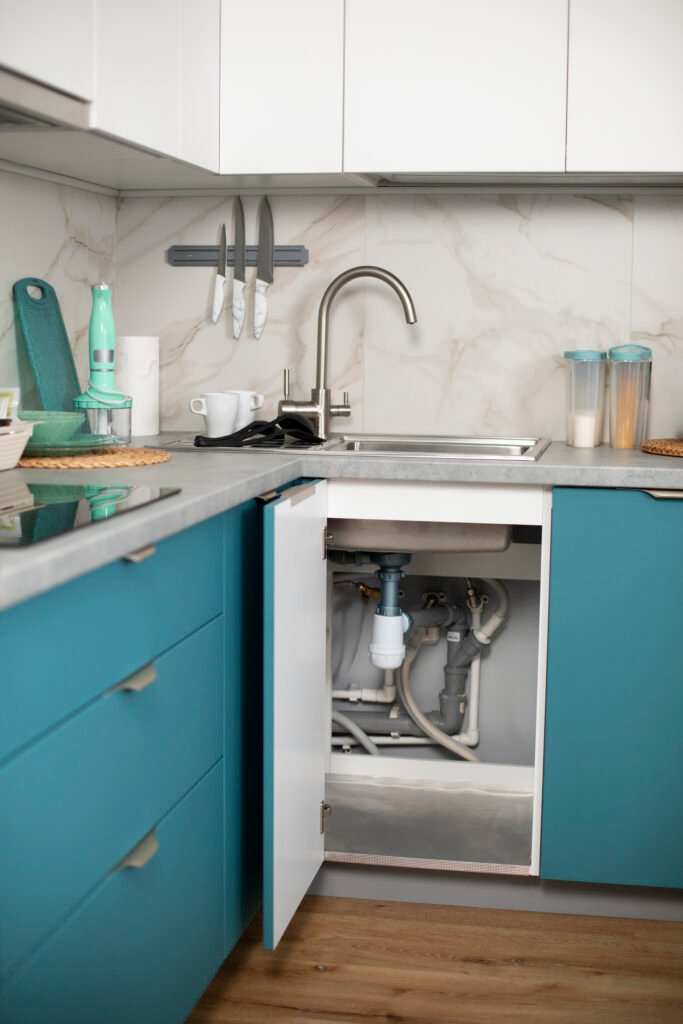 Exposed plumbing pipes beneath a kitchen sink inside the cabinet